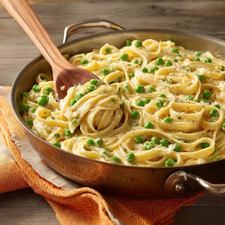 Cremige Fettuccine mit Erbsen, serviert in einer Pfanne mit einem hölzernen Löffel, Nahaufnahme der cremigen Sauce und Pasta.
