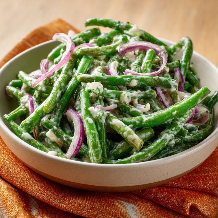 Grüne Bohnen Salat mit cremigem Dressing in einer Schüssel, Nahaufnahme des cremigen Dressings und der roten Zwiebeln.