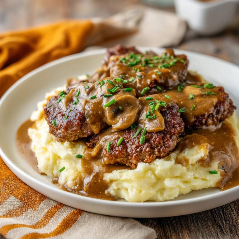 Hacksteaks mit Pilzrahmsoße auf Kartoffelpüree, garniert mit Schnittlauch, serviert auf einem weißen Teller.