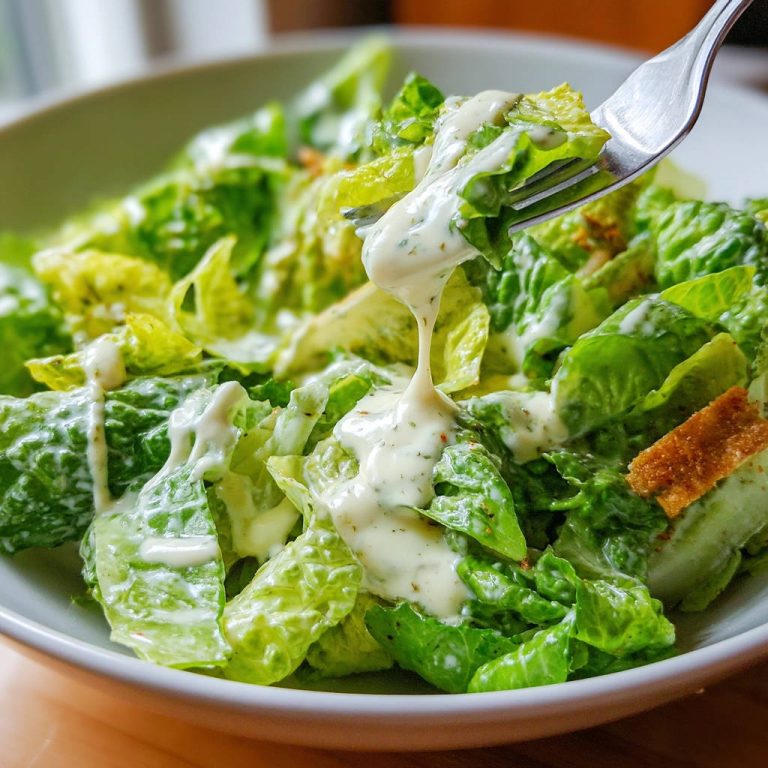 Klassischer Caesar Salat mit cremigem Dressing, das von einer Gabel abtropft und die knackigen Salatblätter umhüllt.