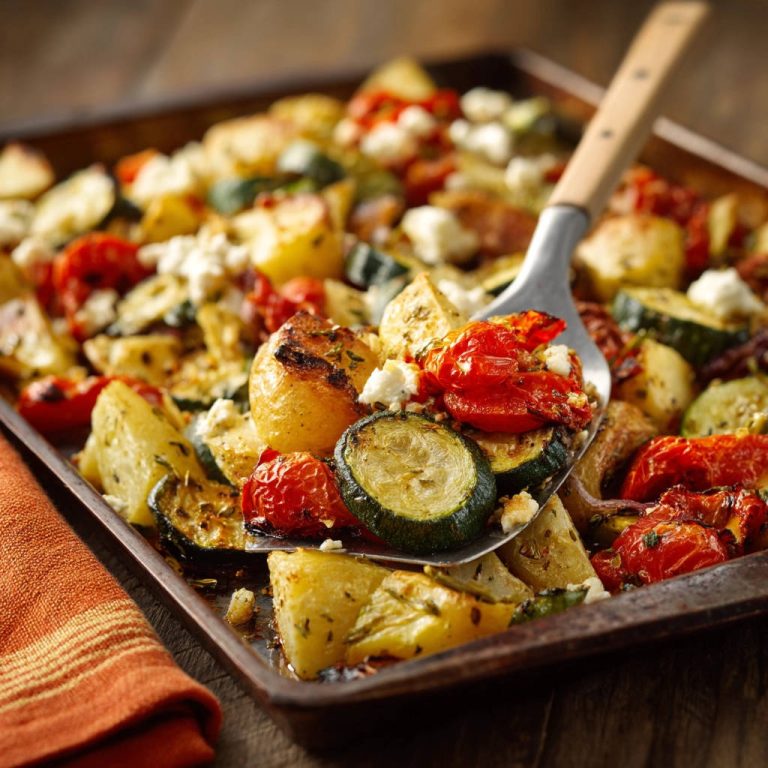 Ofengemüse mit Kartoffeln und Feta auf einem Löffel aus der Auflaufform aufgenommen, mit Fokus auf die gerösteten Zutaten.