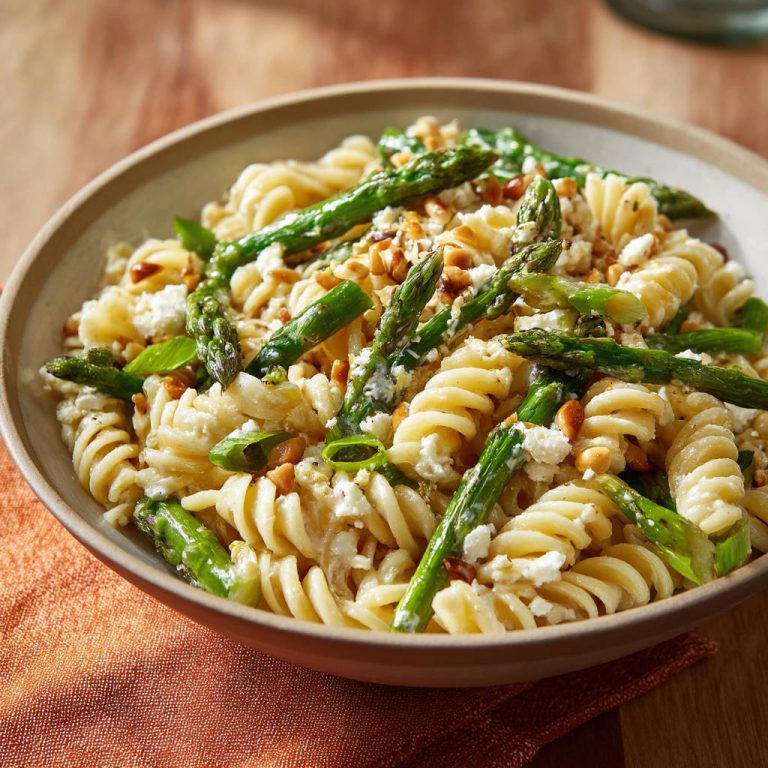 Pasta mit grünem Spargel und Feta als Nahaufnahme in einer Schüssel mit Pinienkernen und Basilikum.