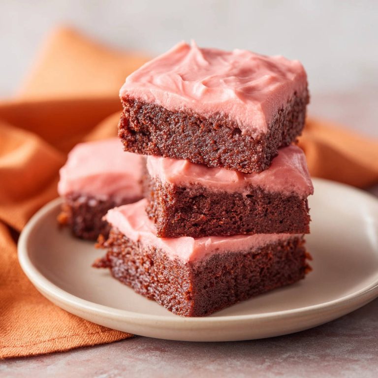 Saftige Schokoladen-Brownies mit Frischkässe-Frosting, gestapelt auf einem Teller mit orangem Tuch im Hintergrund.