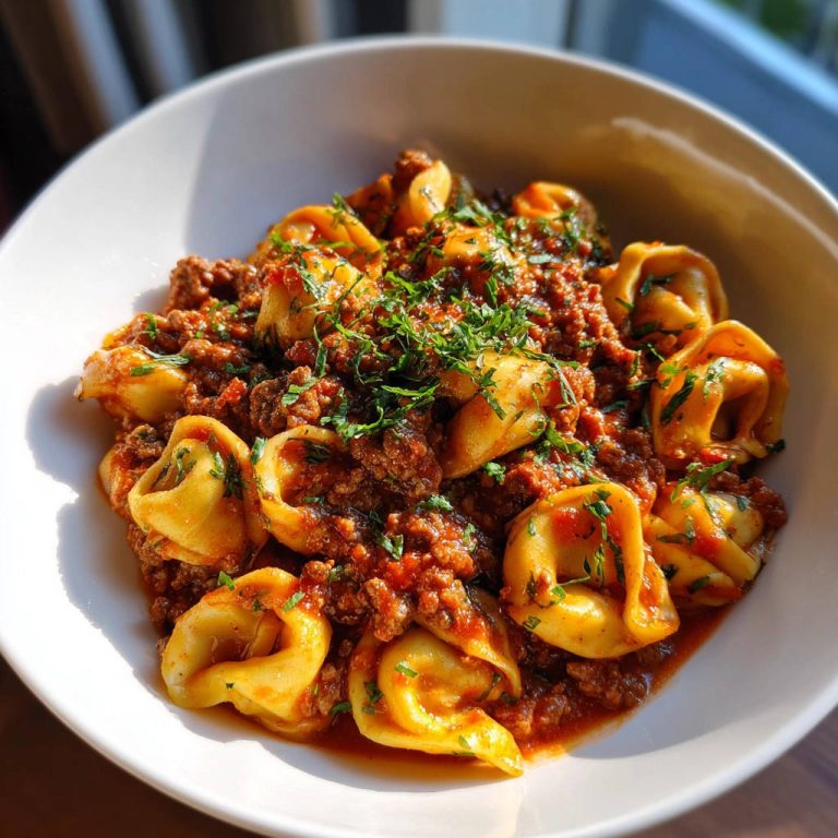 Tortellini mit Fleischsoße als Nahaufnahme in einer weißen Schüssel, garniert mit frischer Petersilie.