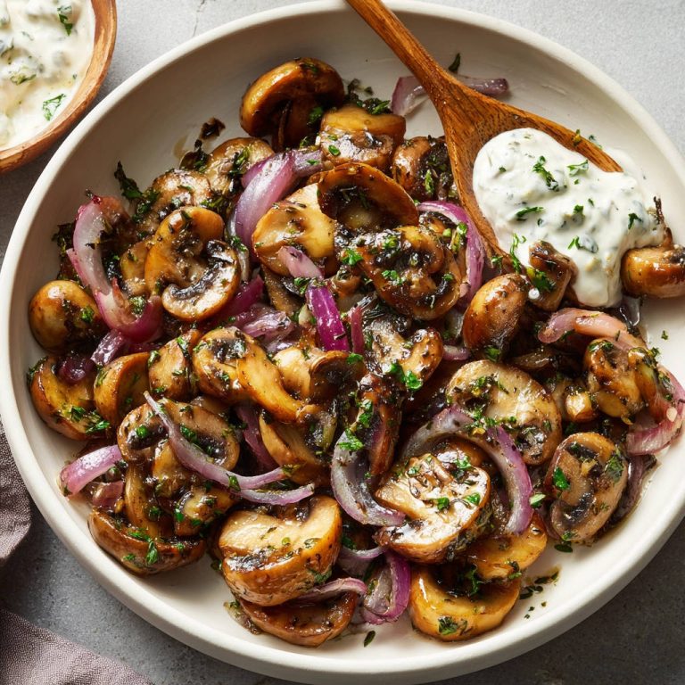 Gebratene Champignons mit roten Zwiebeln und einem Klecks Dip, serviert in einer Schüssel mit Holzlöffel.