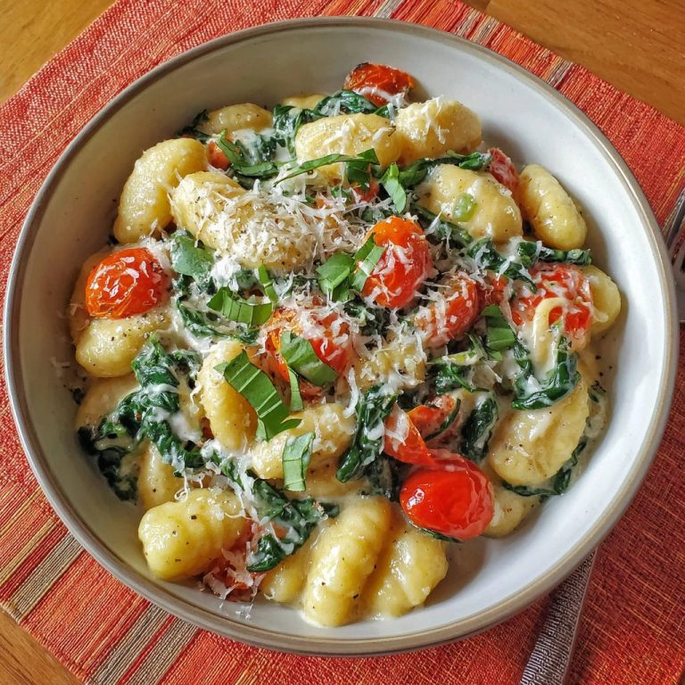 Gnocchi in Cremesauce mit Spinat und Tomaten, serviert in einer Schüssel mit geriebenem Parmesan und frischem Basilikum garniert.