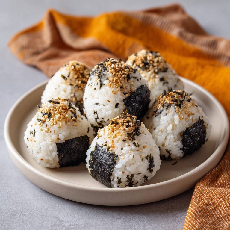 Onigiri mit Sesam und Nori auf einem Teller, garniert mit getoasteten Sesamsamen und zerkleinerter Nori.