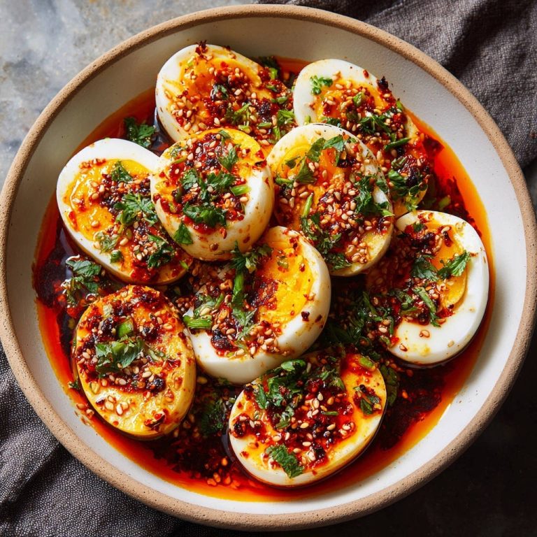Asiatische Chili-Eier, ein Teller mit halbieren gekochten Eiern, üppig garniert mit Chiliöl und Kräutern.