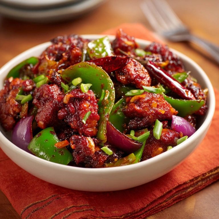 Knuspriges Chili-Hähnchen in einer Schüssel mit Paprika, Zwiebeln und getrockneten Chilis, Nahaufnahme mit Fokus auf Textur.