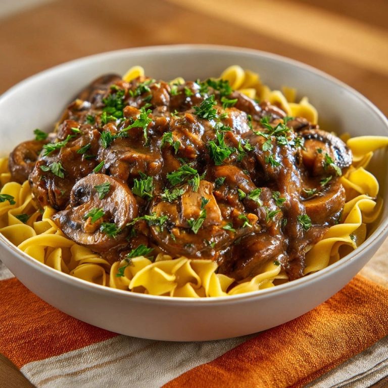 Cremiges Pilz-Ragout mit Eiernudeln, garniert mit frischer Petersilie, in einer weißen Schüssel serviert.