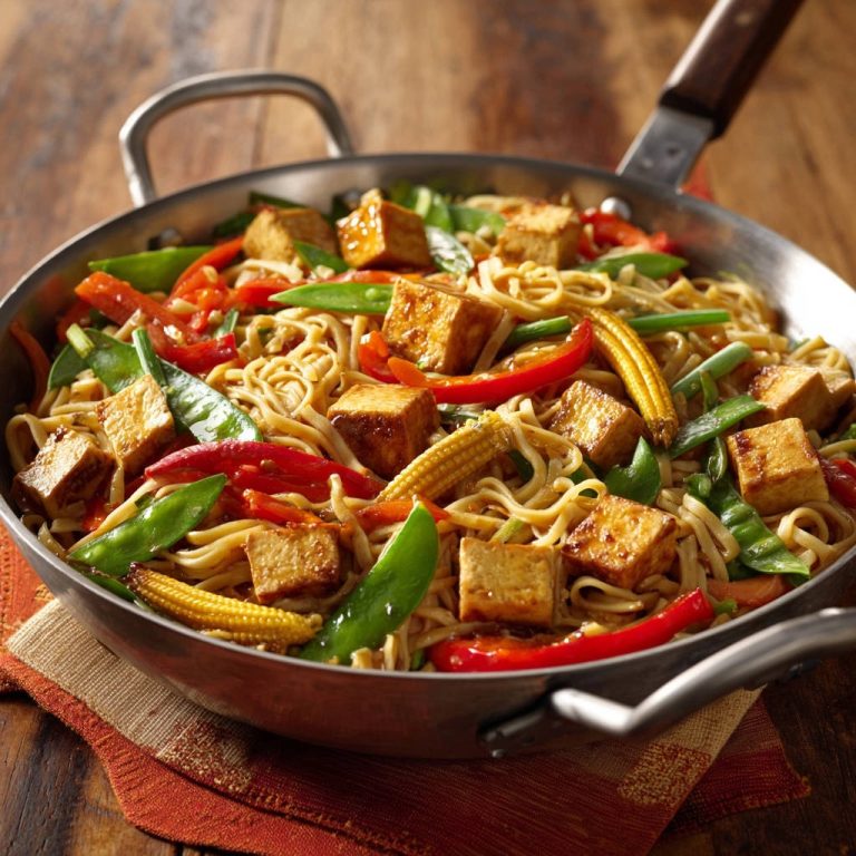 Asiatische Tofu-Nudel-Pfanne mit knackigem Gemüse und Babymais in einer Metallpfanne von nah aufgenommen.