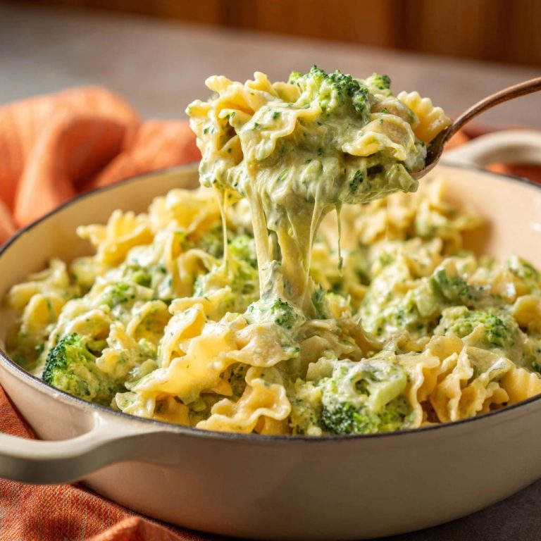 Cremige Brokkoli-Farfalle mit geschmolzenem Käse, das von einem Löffel gezogen wird, eine käsige Nahaufnahme.