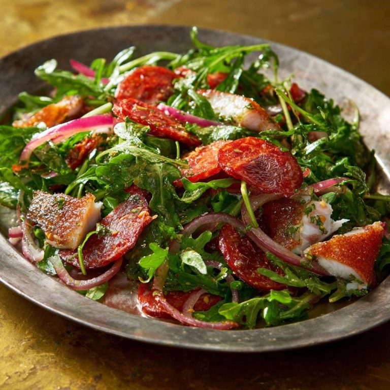 Knuspriger Fischsalat mit pikanten Würzscheiben und Rucola, nahaufnahme der Textur der Zutaten auf einer Servierplatte.
