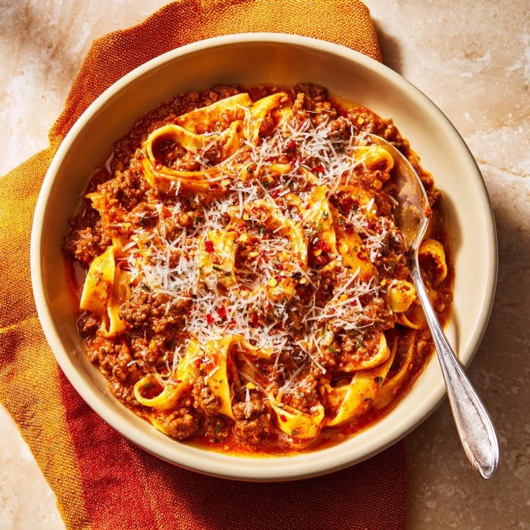 Herzhafte Pappardelle Bolognese von oben mit einem Löffel in einer Schüssel, bestreut mit Parmesan und Chiliflocken.
