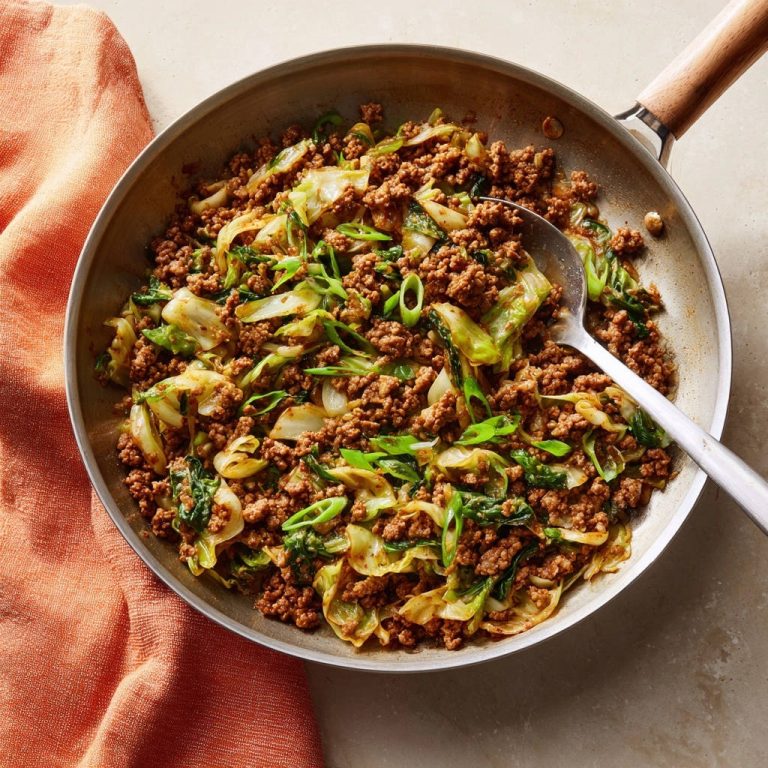 Würzige Hackfleischpfanne mit Kohl, frisch zubereitet und in einer Edelstahlpfanne mit einem Löffel serviert