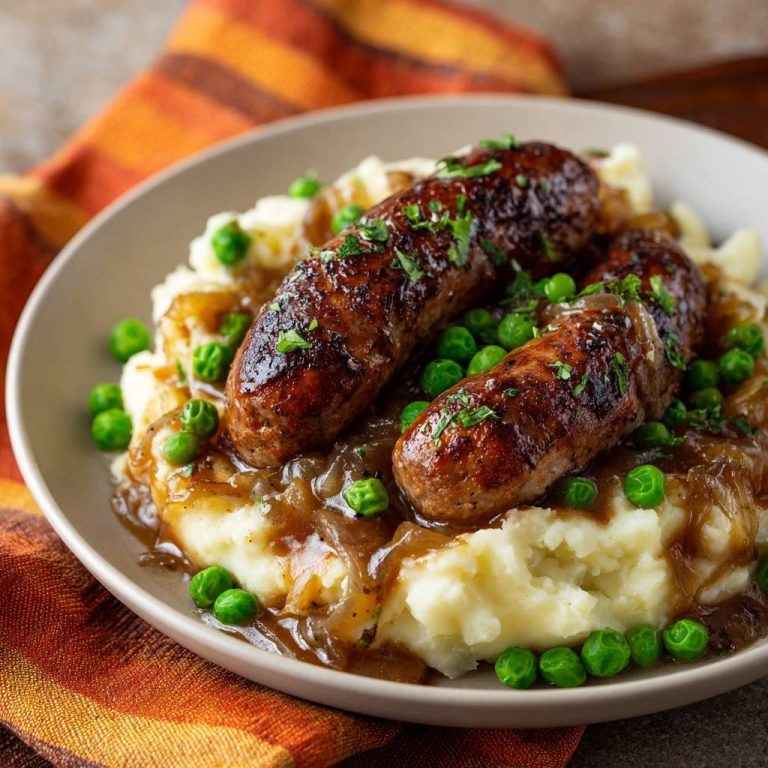 Bratwürste mit Kartoffelbrei, Erbsen und Zwiebelsoße, serviert auf einem Teller in einer Nahaufnahme.