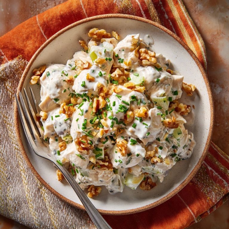Cremiger Hähnchensalat mit Walnüssen und Schnittlauch, garniert mit frischen Kräutern und Nüssen, auf einem Teller serviert.