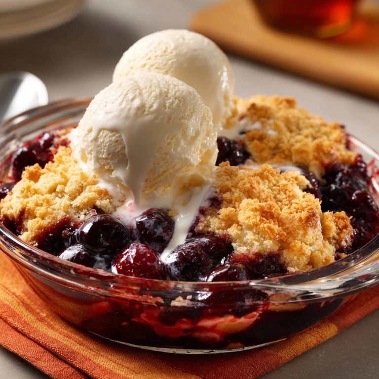 Knuspriger Heidelbeer-Crumble mit Vanilleeis in einer Glasschale, Nahaufnahme mit schmelzendem Eis