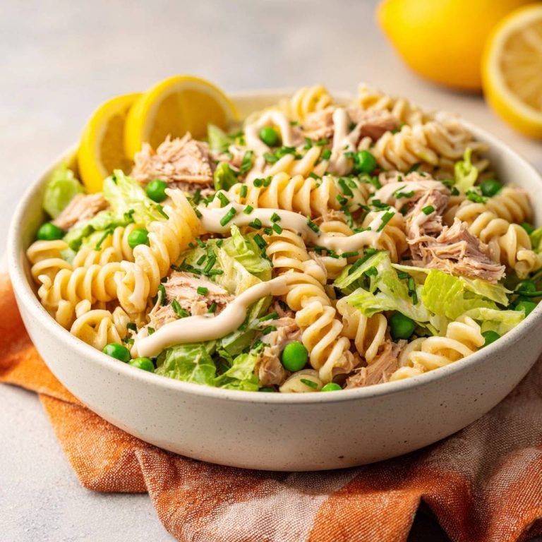Frischer Thunfisch-Fusilli-Salat als Nahaufnahme mit Zitronenspalten und frischen Kräutern garniert auf einem Teller.