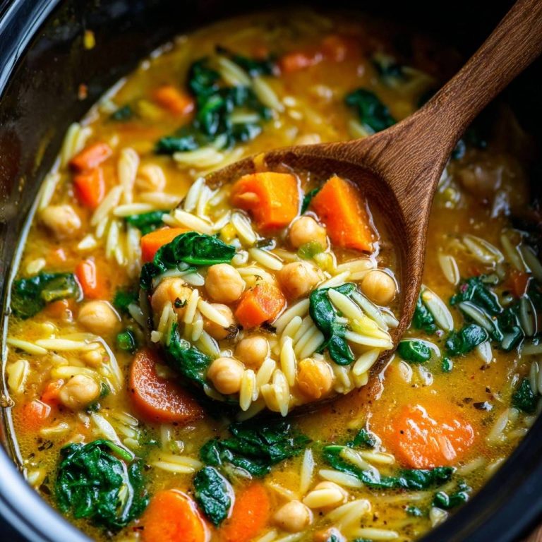 Slowcooker-Orzo-Eintopf mit Kichererbsen, Karotten und Spinat, nah aufgenommen mit einem Holzloeffel zum Servieren.