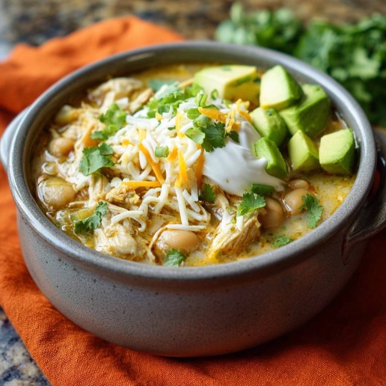 Cremiges Hähnchen-Weißbohnen-Chili, garniert mit Avocado, Sauerrahm, Käse und Koriander in einer Schüssel