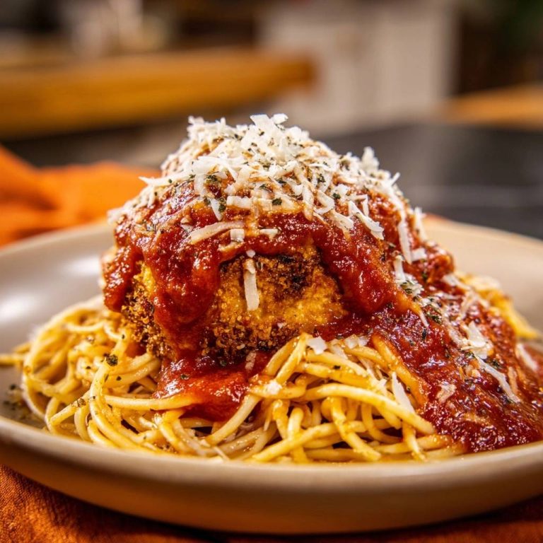 Knuspriges Hähnchen auf Spaghetti, serviert mit Tomatensauce und Parmesan, in einer Nahaufnahme auf einem Teller.