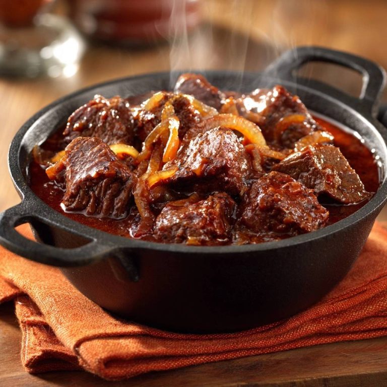 Saftiges Rindergulasch mit Zwiebeln, dampfend heiss in einer schwarzen gusseisernen Pfanne serviert.