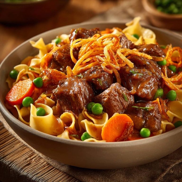 Zartes Rindfleischgulasch mit Nudeln, Karotten und Erbsen, garniert mit knusprigen Zwiebelringen, in einer Schüssel serviert.