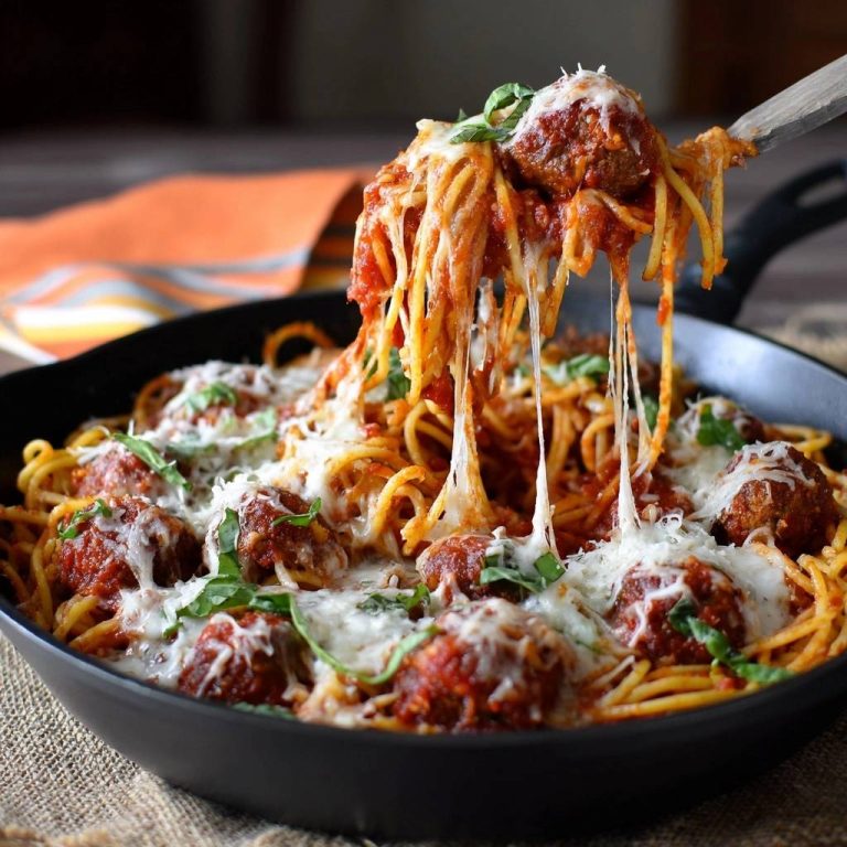 Spaghetti mit saftigen Fleischbällchen, überbacken mit geschmolzenem Käse und garniert mit frischem Basilikum, auf einem Löffel serviert.