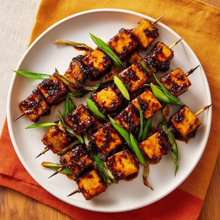Knusprige Teriyaki-Tofu-Spieße mit glänzender Glasur und Frühlingszwiebeln auf einem Teller angerichtet.