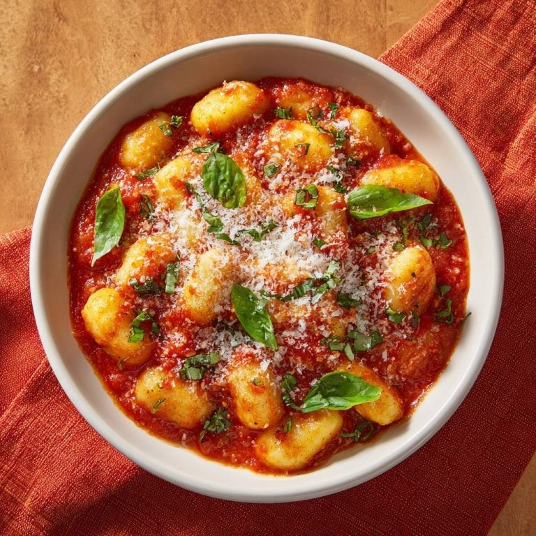 Gnocchi alla Pomodoro von oben mit frischem Basilikum und Parmesan garniert, serviert in einer weißen Schüssel.