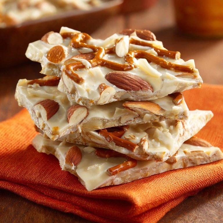 Weiße Schoko-Brezel-Bark mit Mandeln als Nahaufnahme gestapelt auf einem orangefarbenen Tuch.