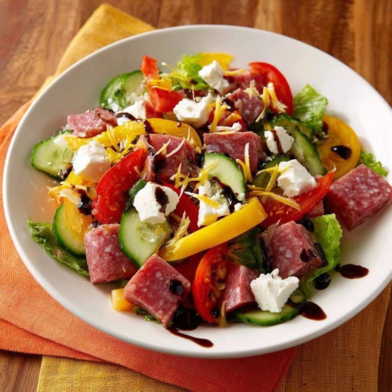 Mediterraner Salami-Feta-Salat serviert in einer weißen Schüssel mit frischen Zutaten und Balsamico-Dressing.