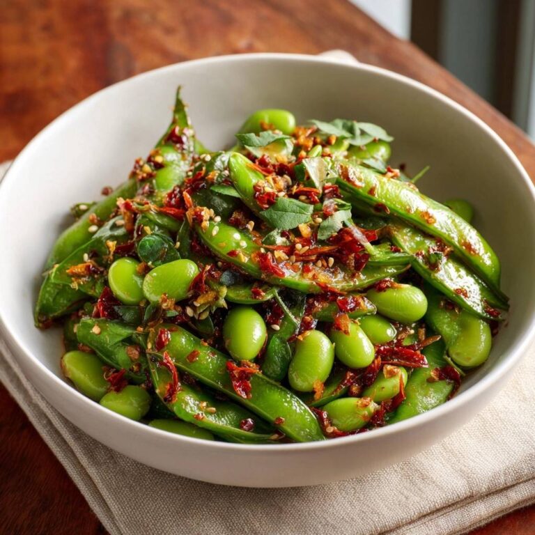 Würzige Chili-Knoblauch-Edamame als Nahaufnahme in einer Schüssel mit frischen Kräutern und Chili-Flocken garniert.